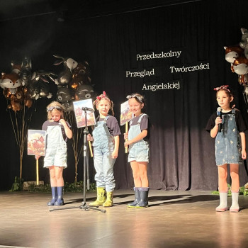 trzy dziewczynki trzymają tabliczki przy jednym mikrofonie obok stoi dziewczynka z mikrofonem